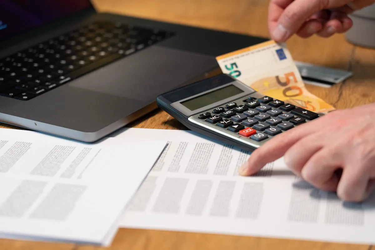 Calculator, euro banknote and papers next to a laptop